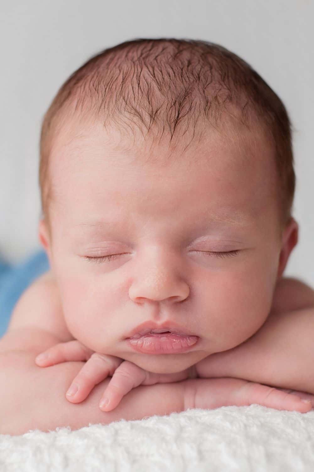 Baby boy with head resting on folded arms.
