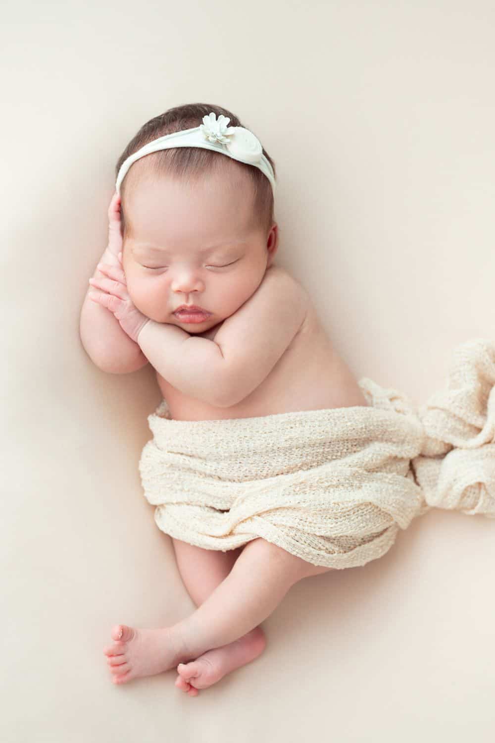 Newborn baby girl with cream headband and cloth wrap around waist. Pretty girl names that start with S.