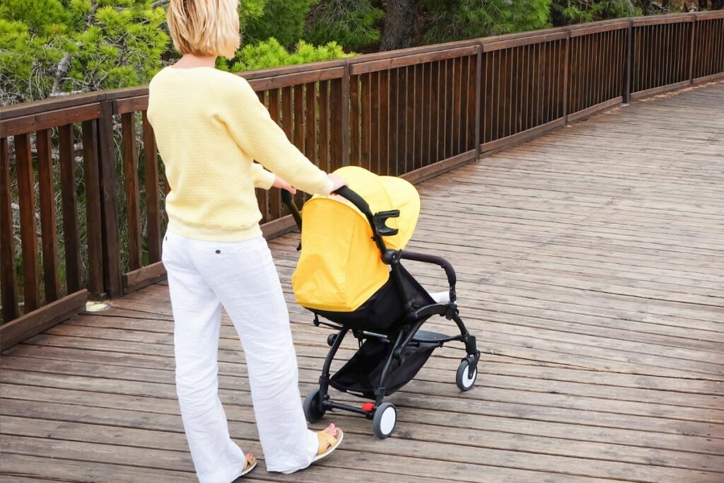 Mother walking baby in stroller on boardwalk.