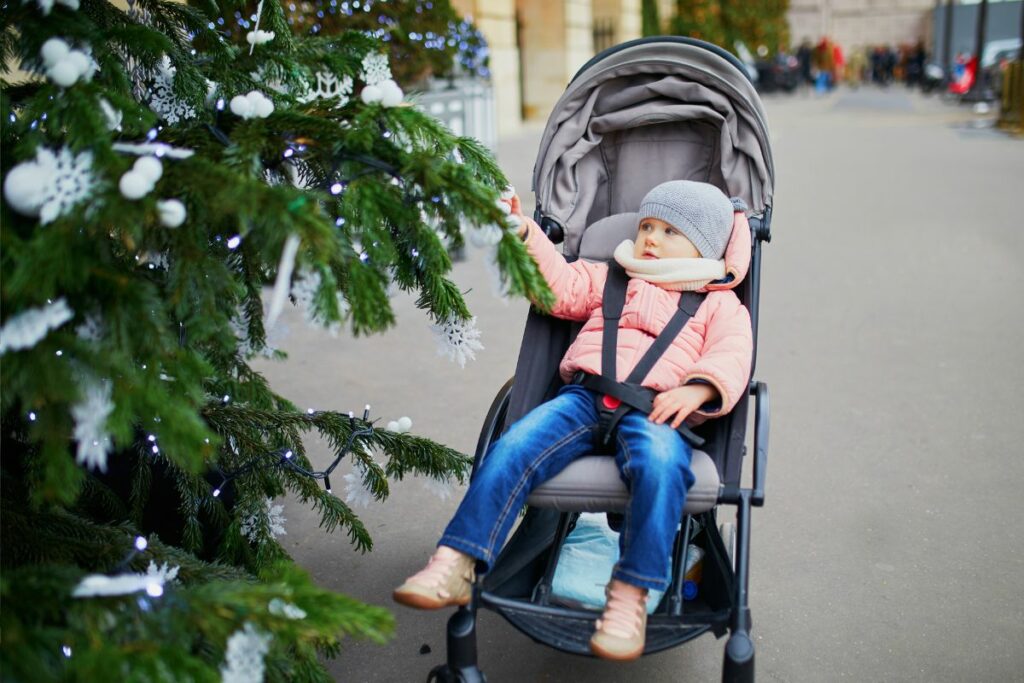 Bigger child in a stroller reaching out for Christmas tree.