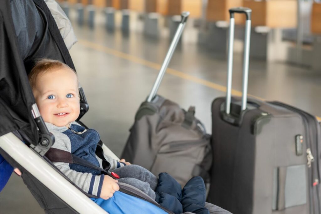 Baby sitting in stroller at airport with luggage.