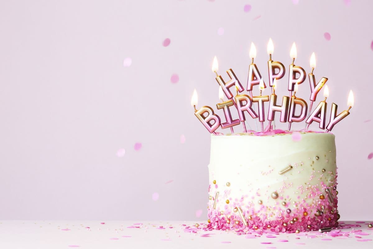 A pink and white birthday cake decorated with gold and pink “Happy Birthday” candles and pink confetti, symbolizing joyful birthday wishes for a daughter.