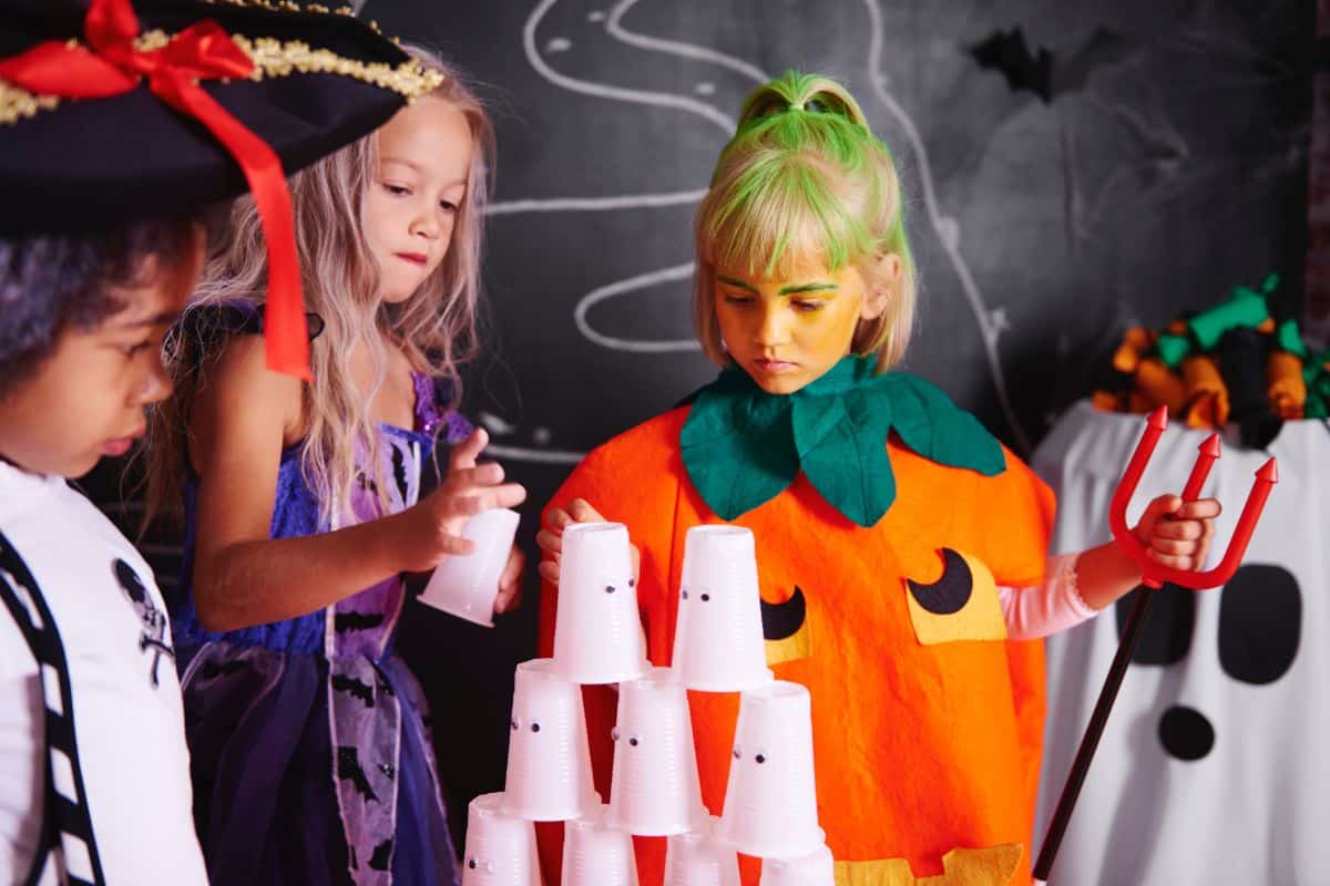 Three young children in Halloween costumes play a party game indoors.